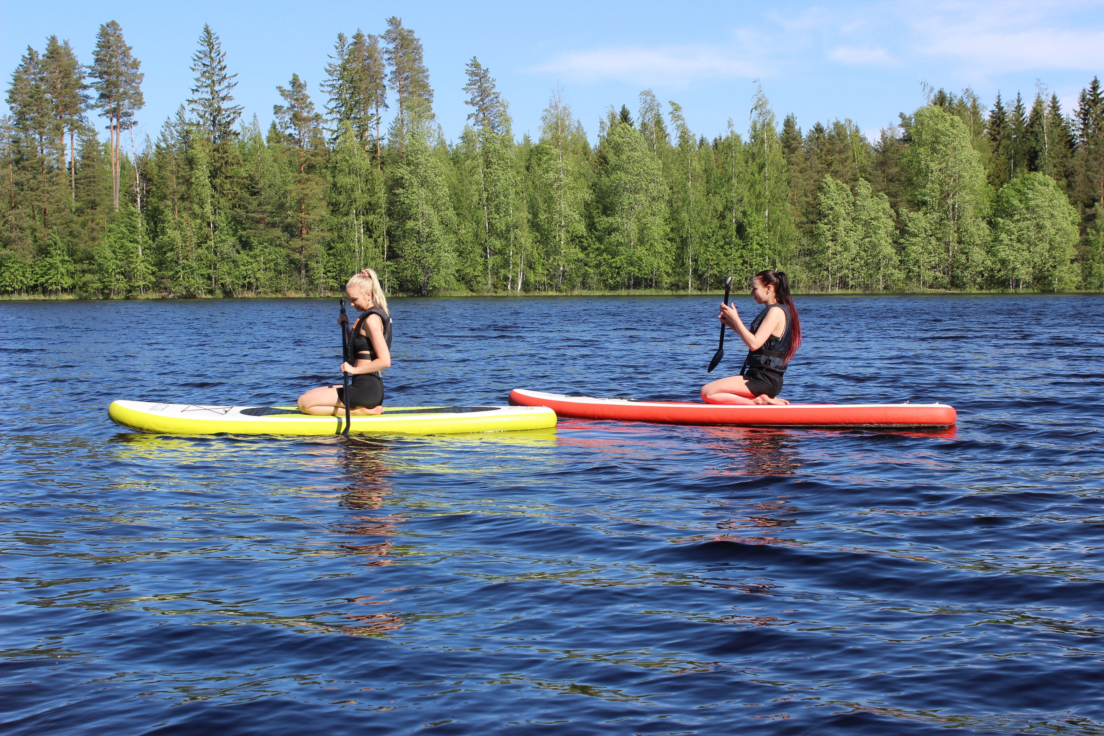 Dos personas en tablas de paddleboard sobre un lago tranquilo rodeado de un bosque denso.