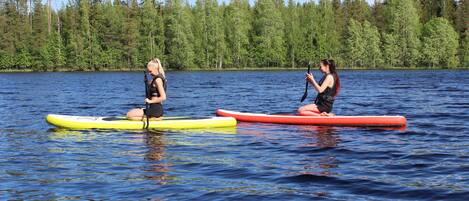 Dos personas en tablas de paddleboard sobre un lago tranquilo rodeado de un bosque denso.