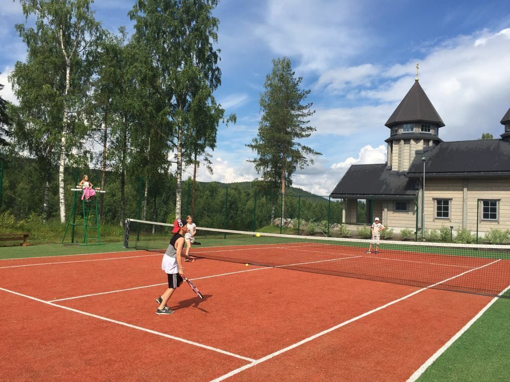 A tennis court with players, surrounded by trees and a building with a tower.