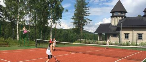 A tennis court with players, surrounded by trees and a building with a tower.