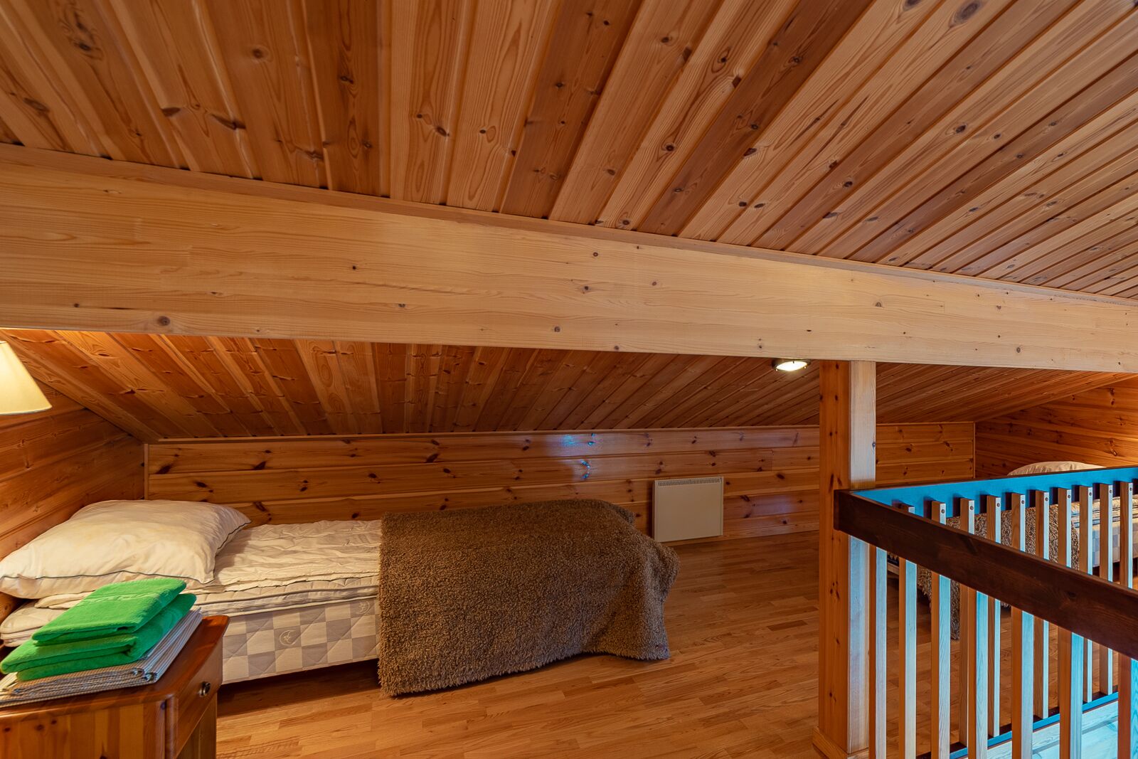 Une chambre confortable avec un plafond en bois, un lit doté d’un matelas à carreaux, une couverture et une petite table de chevet avec une lampe.
