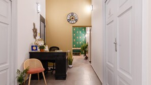 A hallway with a reception desk, a clock, and a green wall with a pattern. - Monteoliveto 33 (Naples)