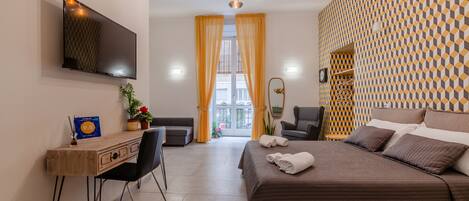 A modern hotel room with a bed, desk, chair, and a TV on the wall.