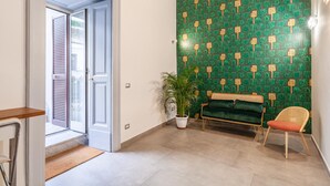 A hallway with a green patterned wall, a bench, a chair, and a potted plant. - Monteoliveto 33 (Naples)