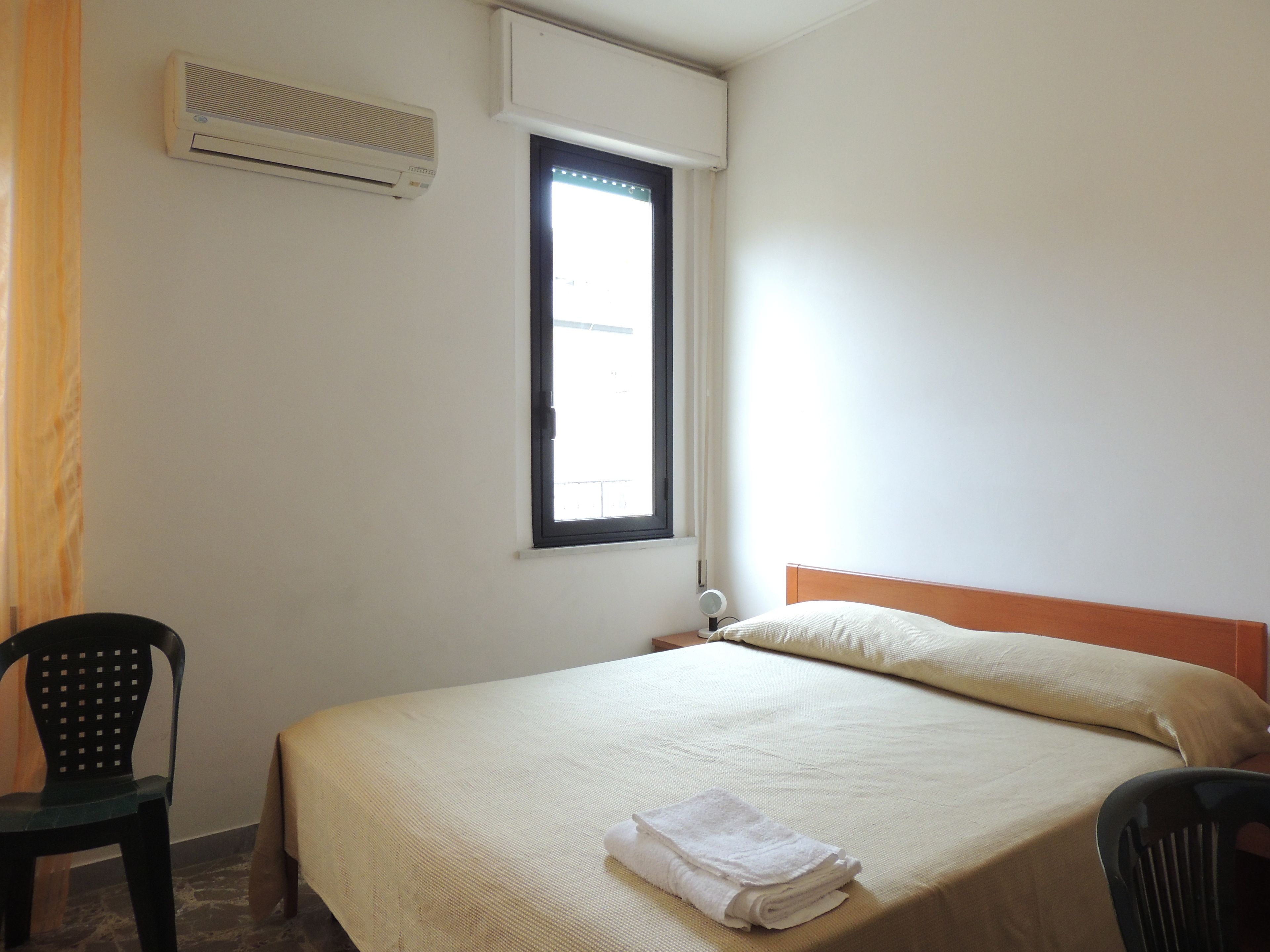Une pièce avec un lit, une fenêtre, un climatiseur et deux chaises.