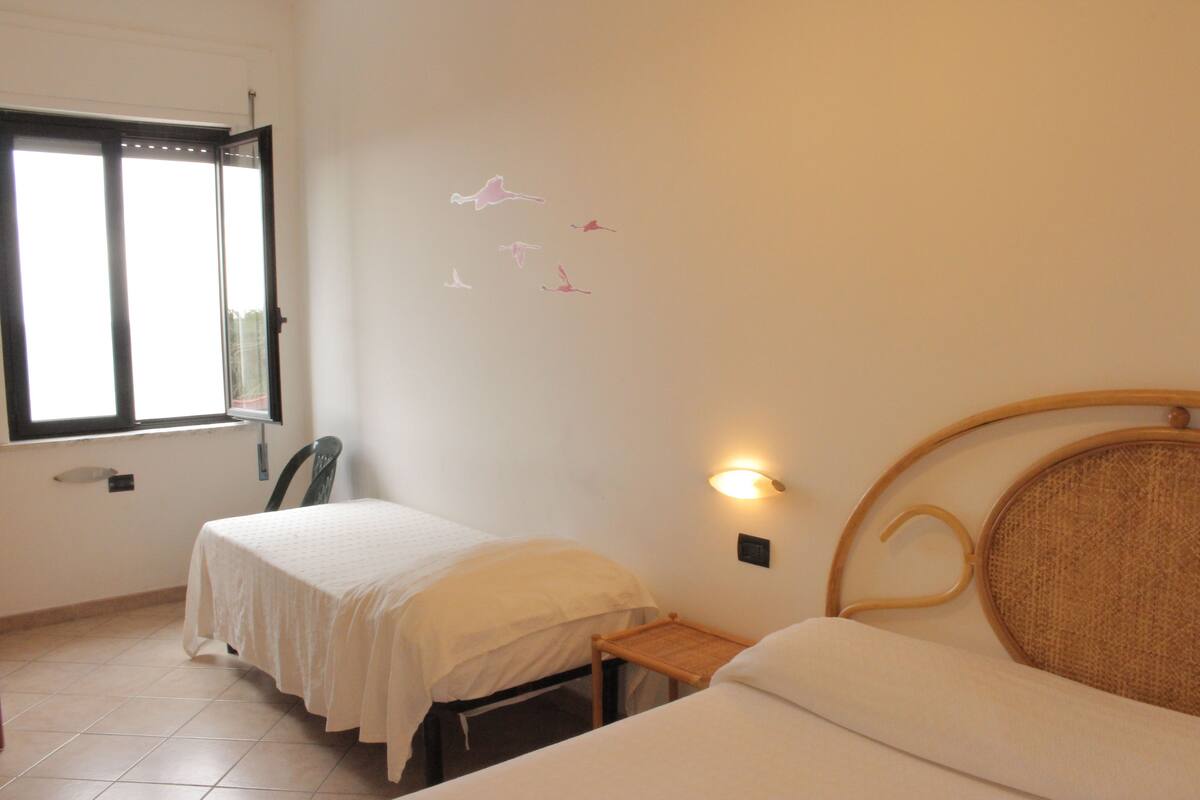 A bedroom with two beds, a window, and a wall-mounted light fixture.