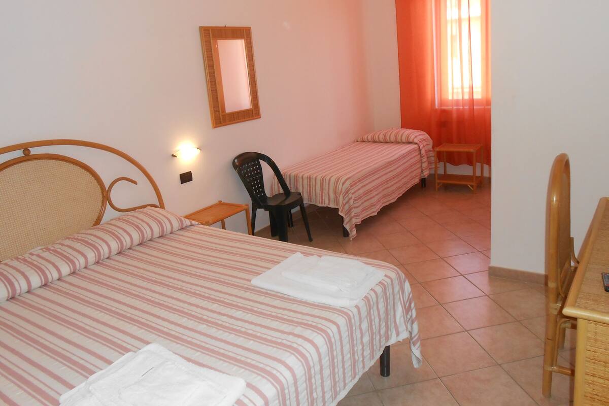 A room with two single beds, a chair, a small table, and a mirror on the wall.