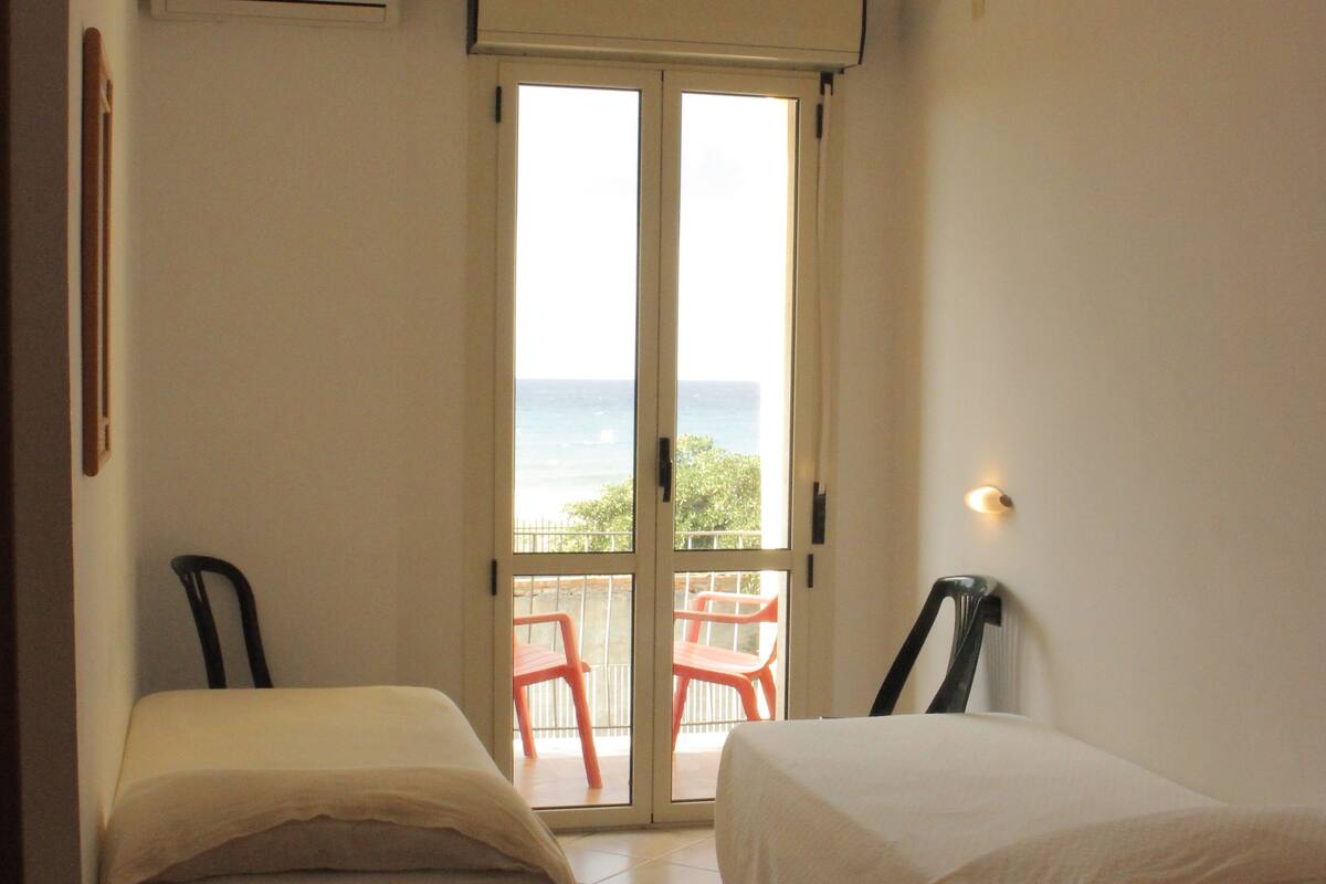 A room with two beds, a balcony with a view, and a ceiling light.