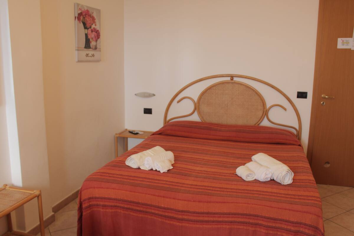 A neatly made bed with a striped bedspread and two rolled towels on it.