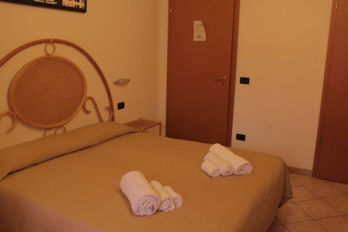 A hotel room with a bed, a wooden headboard, a small table, and a door.