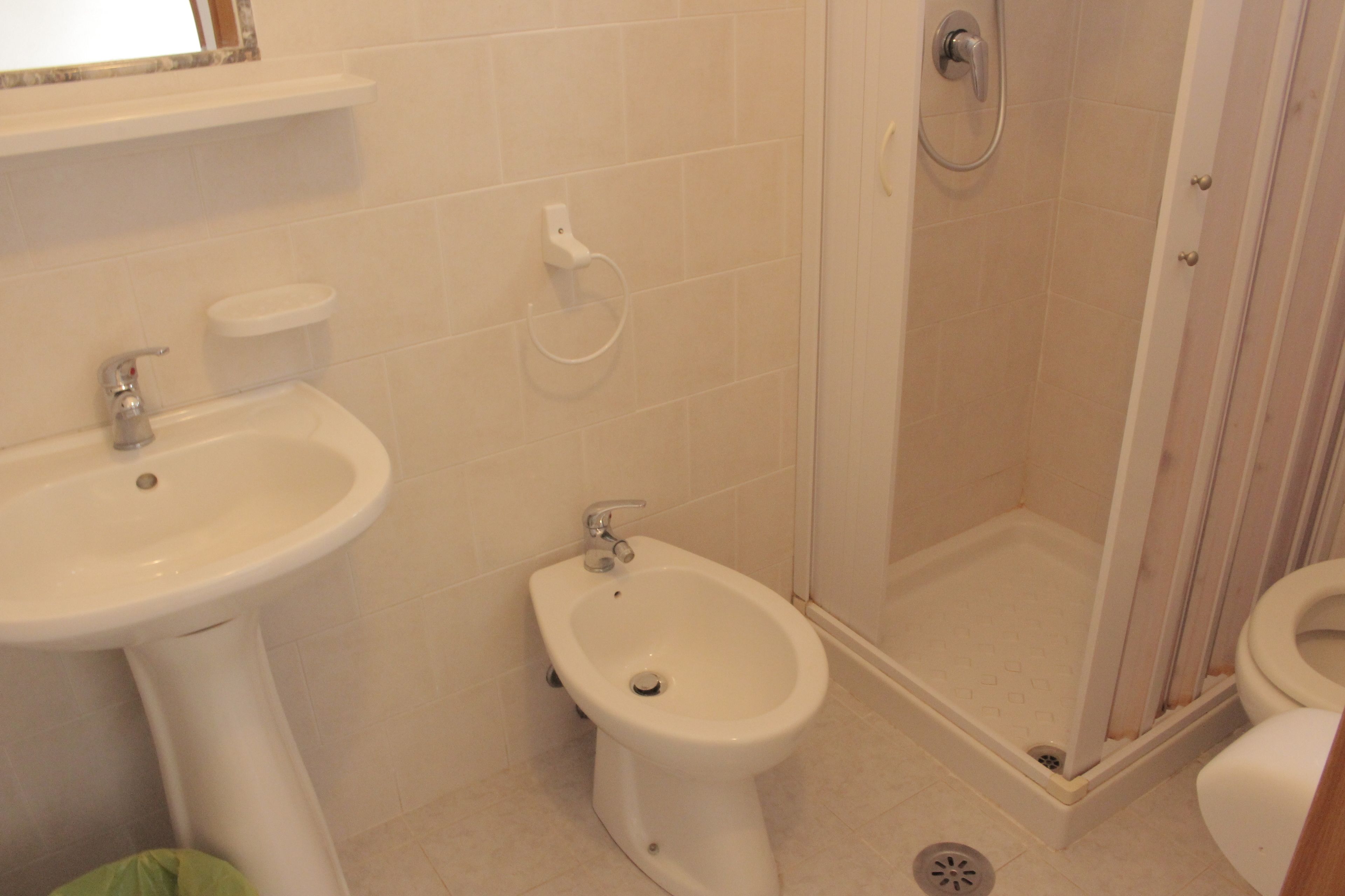 Un baño con lavamanos pedestal, un bidé, cabina de ducha y retrete.