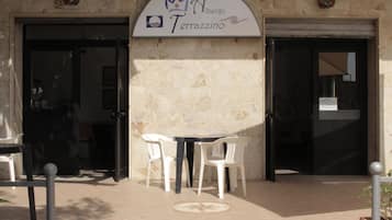 Ein Sitzbereich im Freien mit Tisch und Stühlen vor einem Gebäude, an dem ein Schild mit der Aufschrift „Alberto Terrazzo“ angebracht ist.