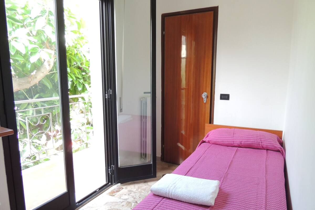 A room with a bed, a door, and a sliding glass door leading to a balcony.