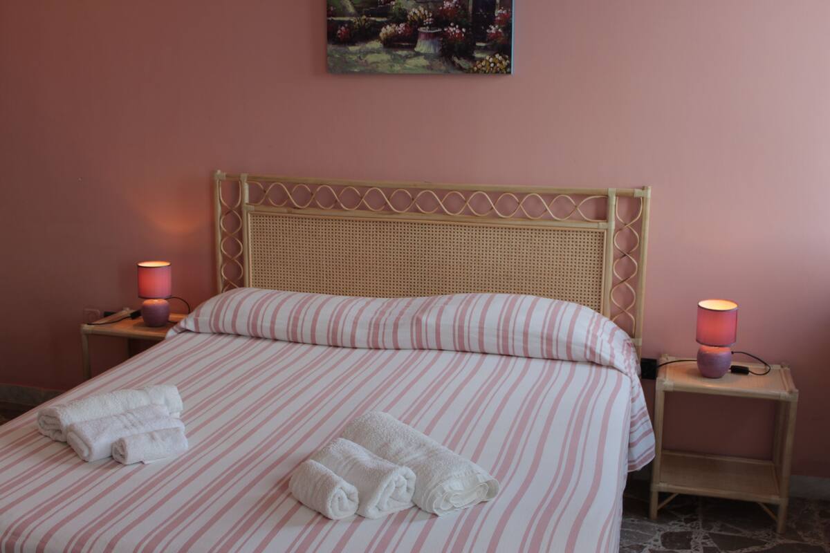 A neatly made bed with striped bedding and two rolled towels on the bed. There are two bedside tables with lamps on either side of the bed.