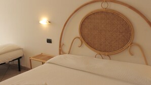A neatly made bed with a headboard that includes a circular woven panel, a bedside table, and a wall-mounted light fixture. - Terrazzino (Vibo Valentia)