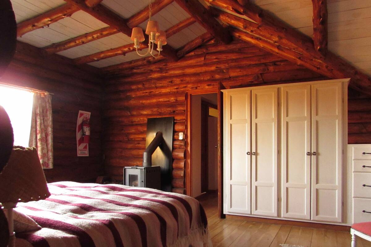 A log cabin bedroom with a bed, wardrobe, and a fireplace.