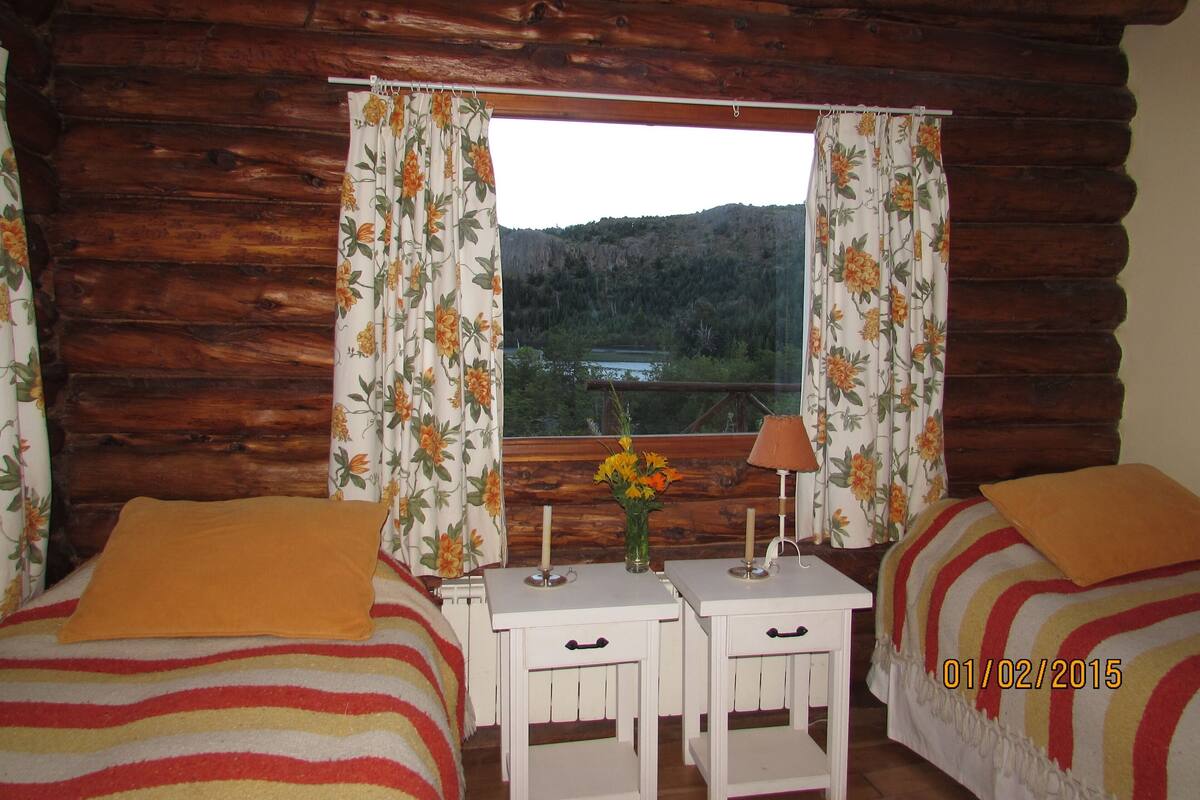 A cabin room with two beds, a small table with a lamp, and a window with curtains.