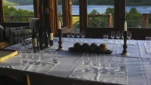 Une table à manger dressée pour un repas, avec des verres à vin, des bouteilles et une bougie, donnant sur un lac.