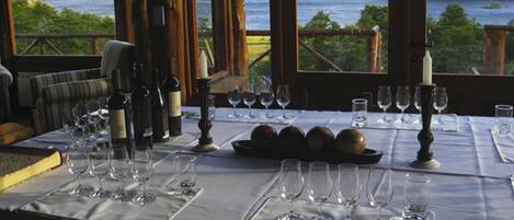 A dining table set for a meal with wine glasses, bottles, and a candle, overlooking a lake.