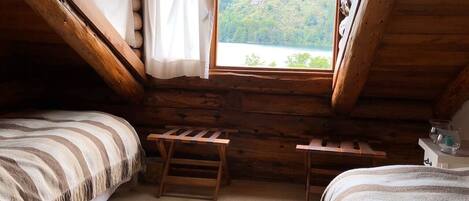 Un chalet confortable avec deux lits, une petite table et une fenêtre donnant sur un lac et des montagnes.