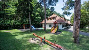 A playground with a seesaw, a slide, and a building with a red roof and yellow stairs.