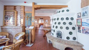 A rustic interior with a brick floor, wicker furniture, and a unique stove with circular knobs. - Abbázia Country Club (Márokföld)