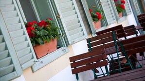 A row of wooden benches and green shutters with potted red flowers on a building facade. - Abbázia Country Club (Márokföld)