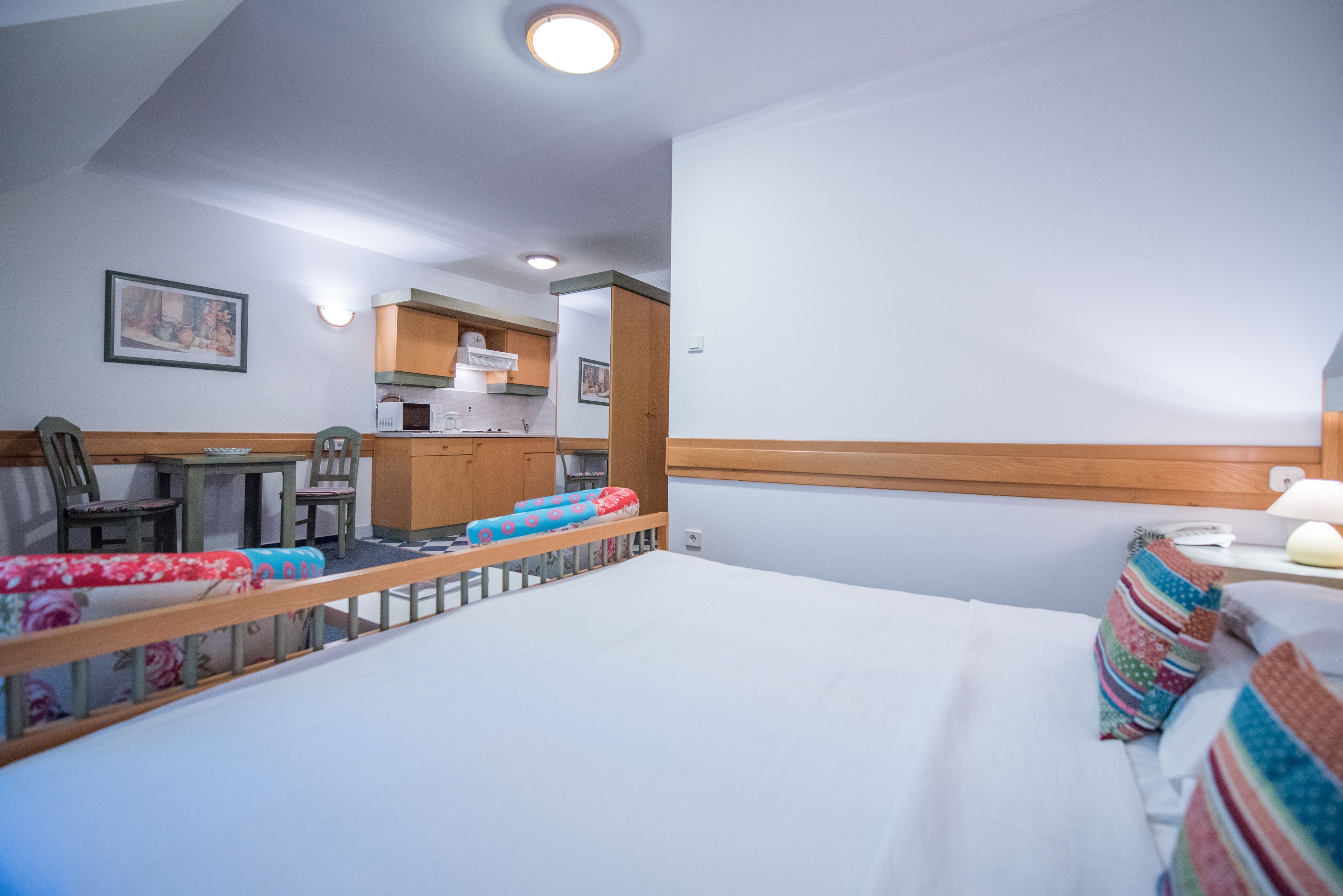 A hotel room with a bed, a small kitchenette, a dining area, and a bathroom.