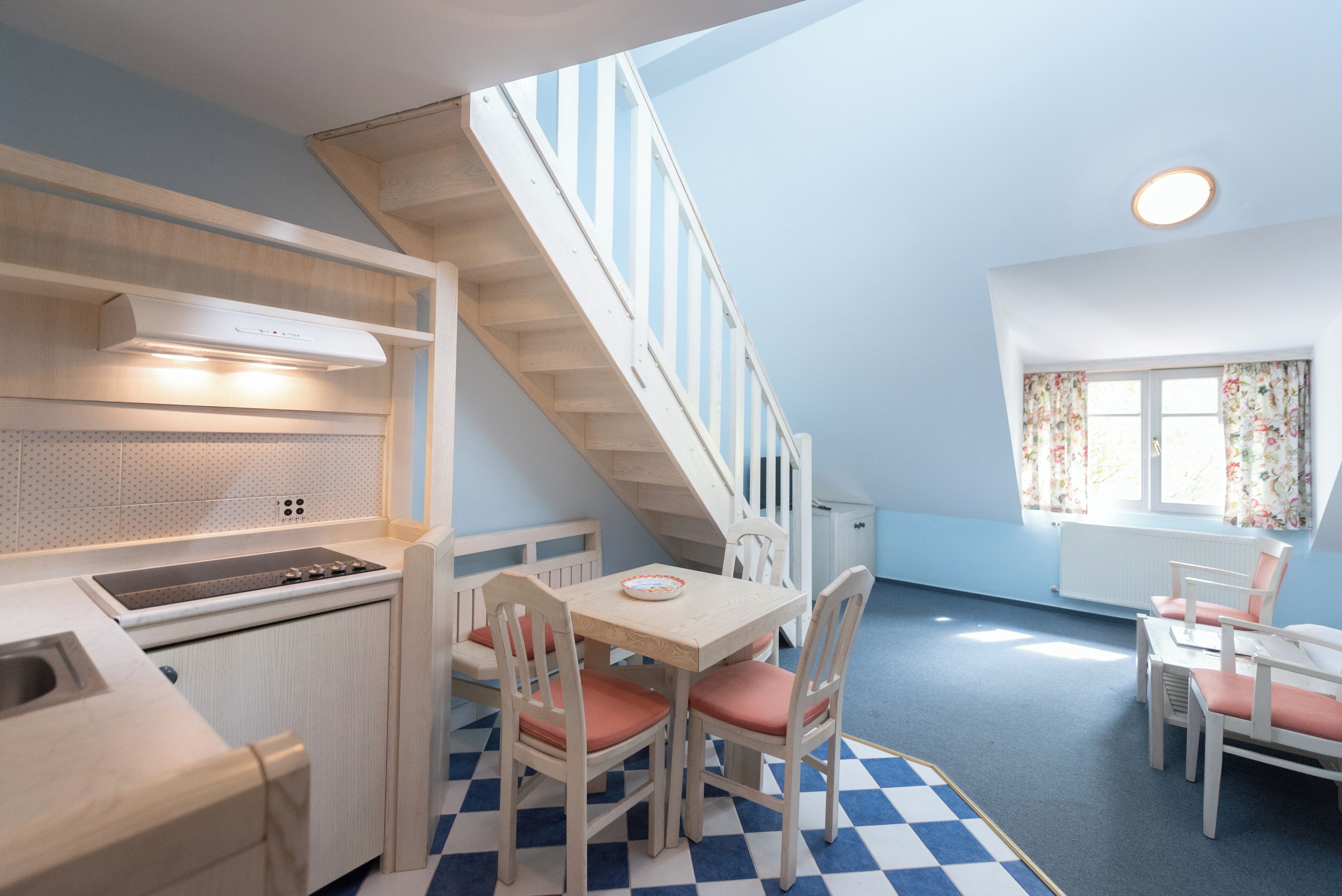 Una cocina compacta con zona de comedor, una escalera y una ventana con cortinas.