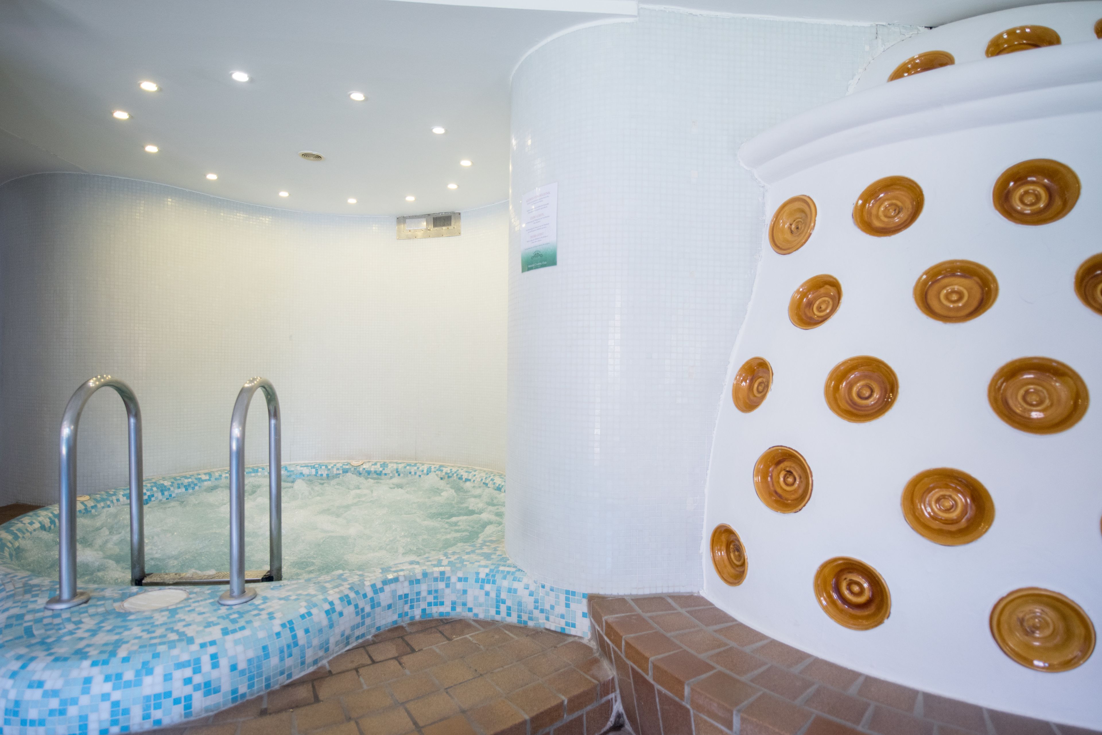 A spa area with a hot tub, a tiled wall, and a large white column with circular patterns.