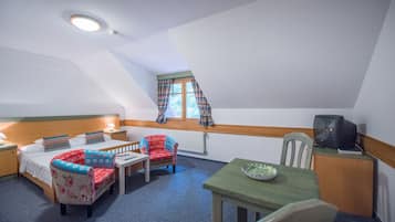Una habitación acogedora con cama, dos sillas, una mesa, televisión y ventana con cortinas escocesas.