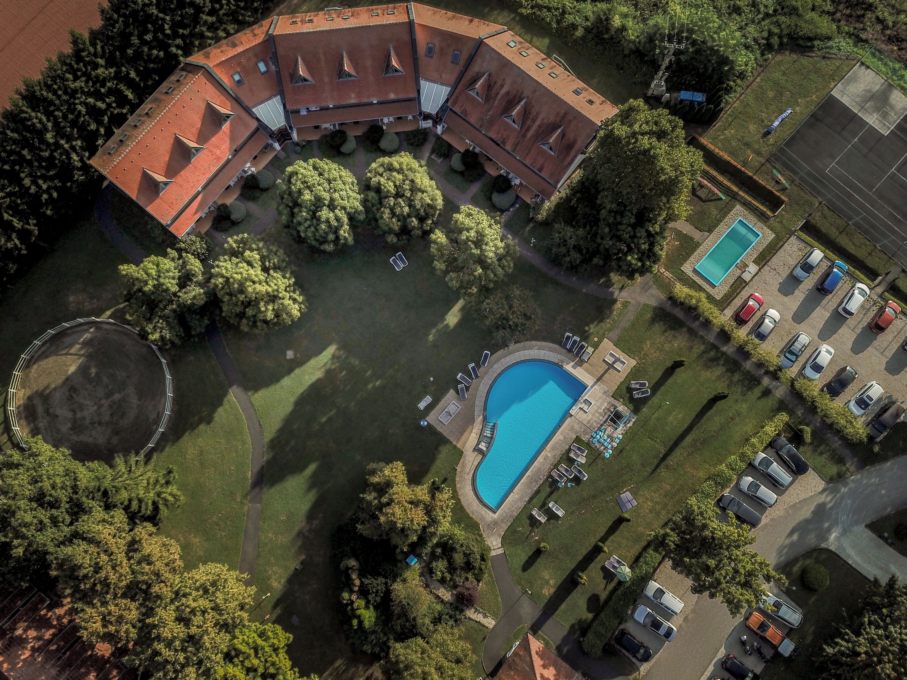 Vista aérea de una propiedad con piscina, zona de estacionamiento y un edificio grande con techo rojo.