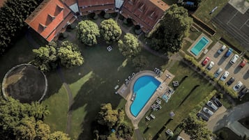Vista aérea de una propiedad con piscina, zona de estacionamiento y un edificio grande con techo rojo.