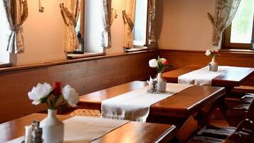 A dining area with wooden tables and benches, white tablecloths, and vases with flowers.