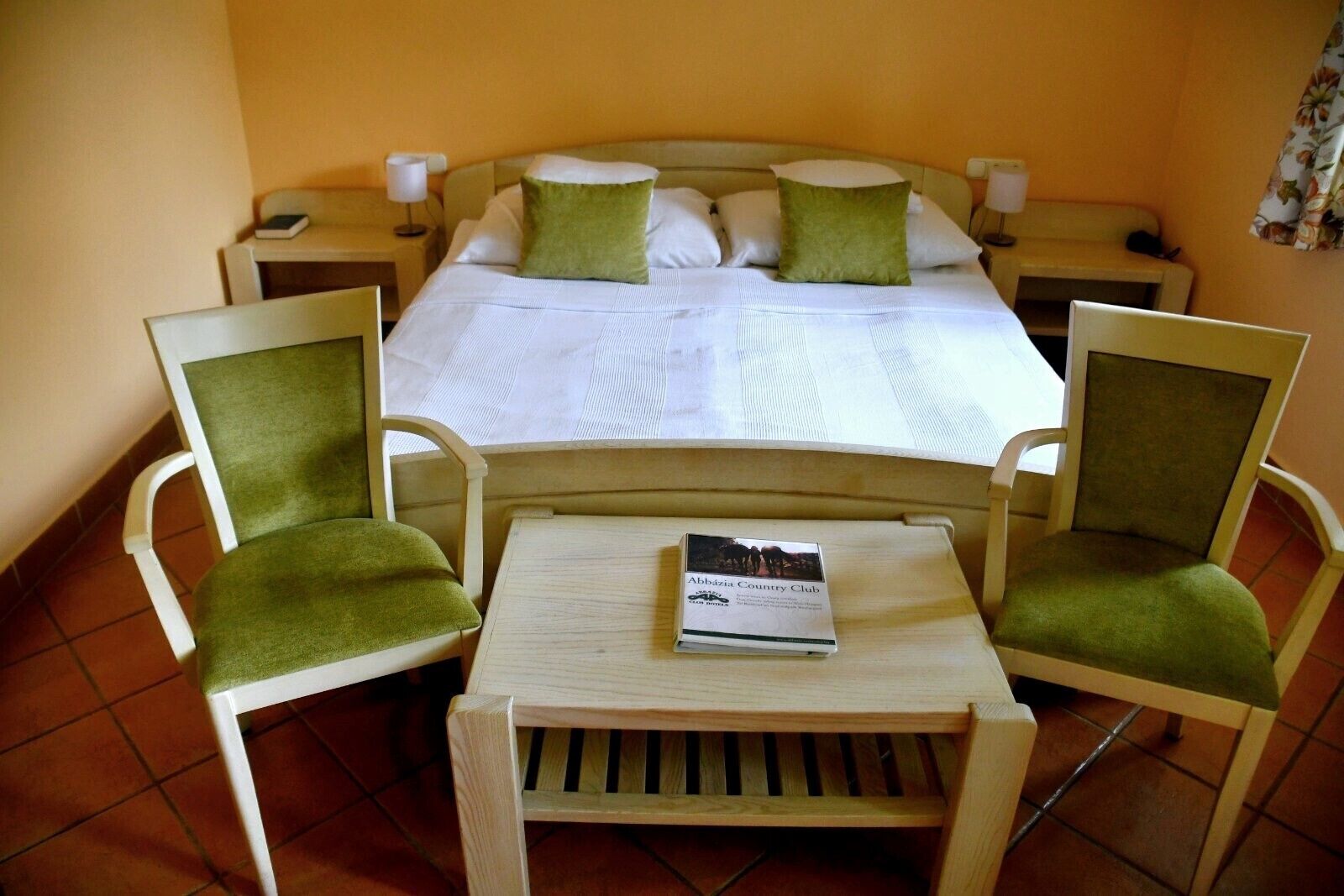 A hotel room with a bed, two nightstands, two chairs, a small table, and a brochure on the table.