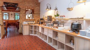 A spacious kitchen with a brick floor, wooden cabinets, and a long counter with various kitchen appliances and utensils. - Abbázia Country Club (Márokföld)