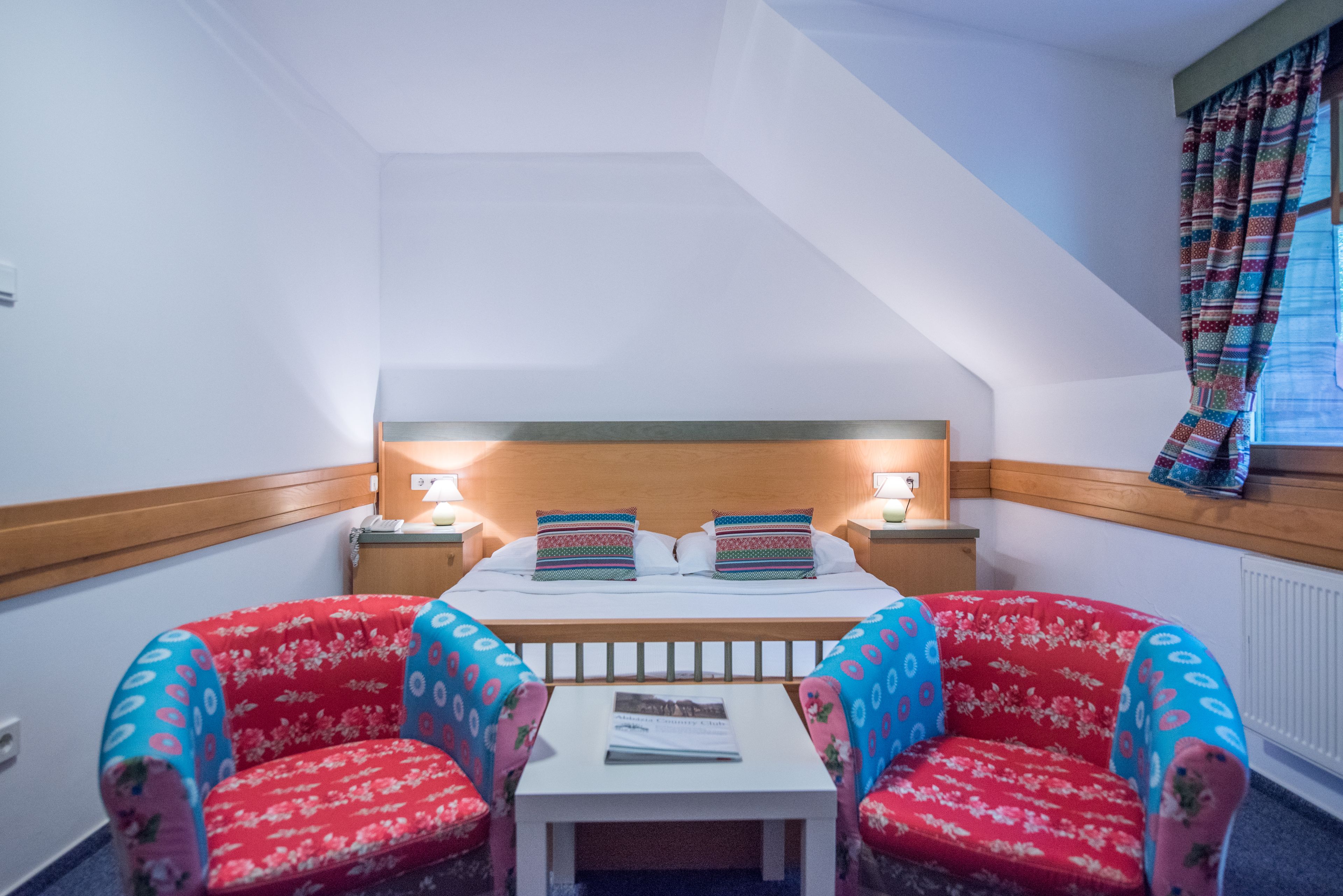 A hotel room with a bed, two nightstands, a table, and two armchairs.