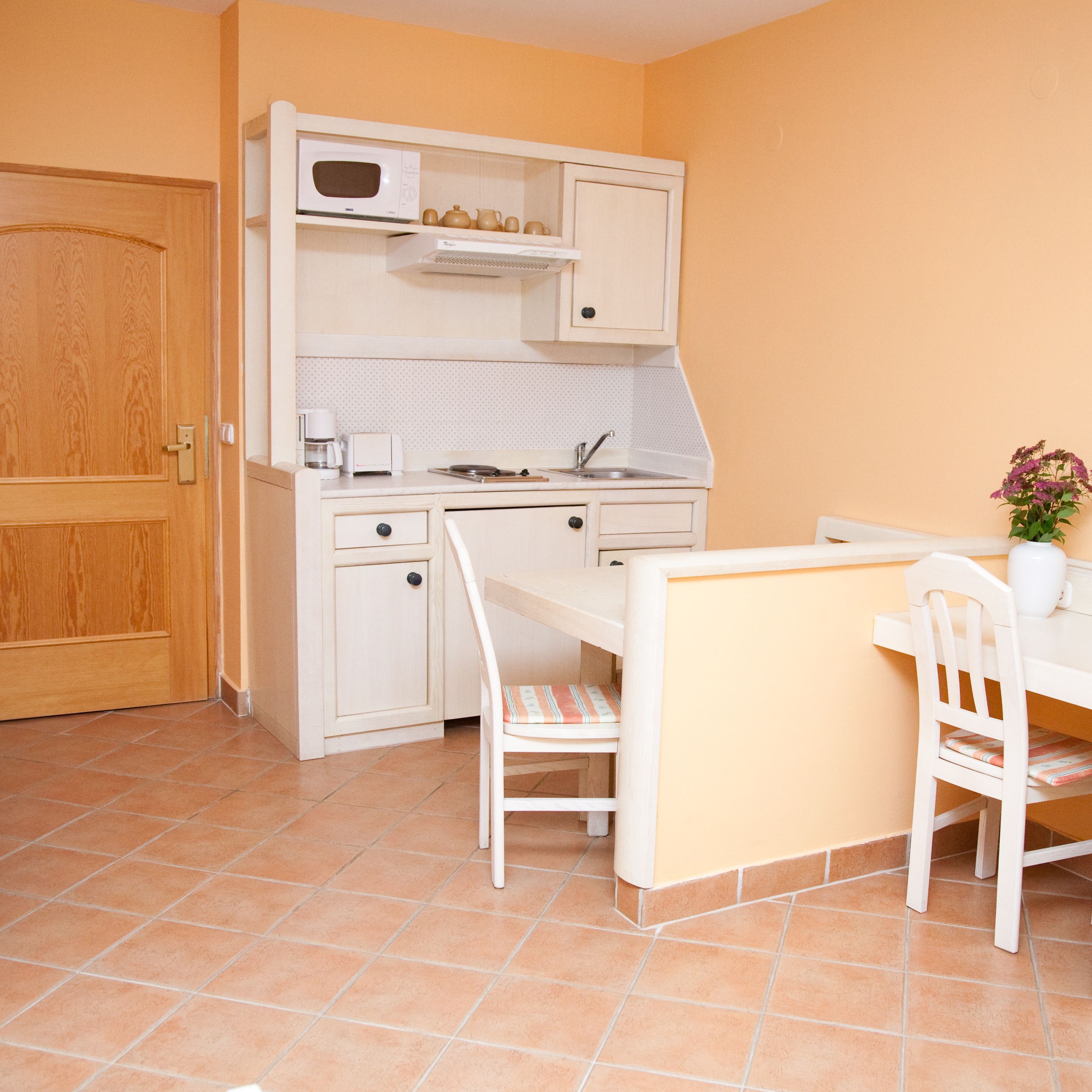 A compact kitchen with a microwave, coffee maker, and a small dining table with chairs.