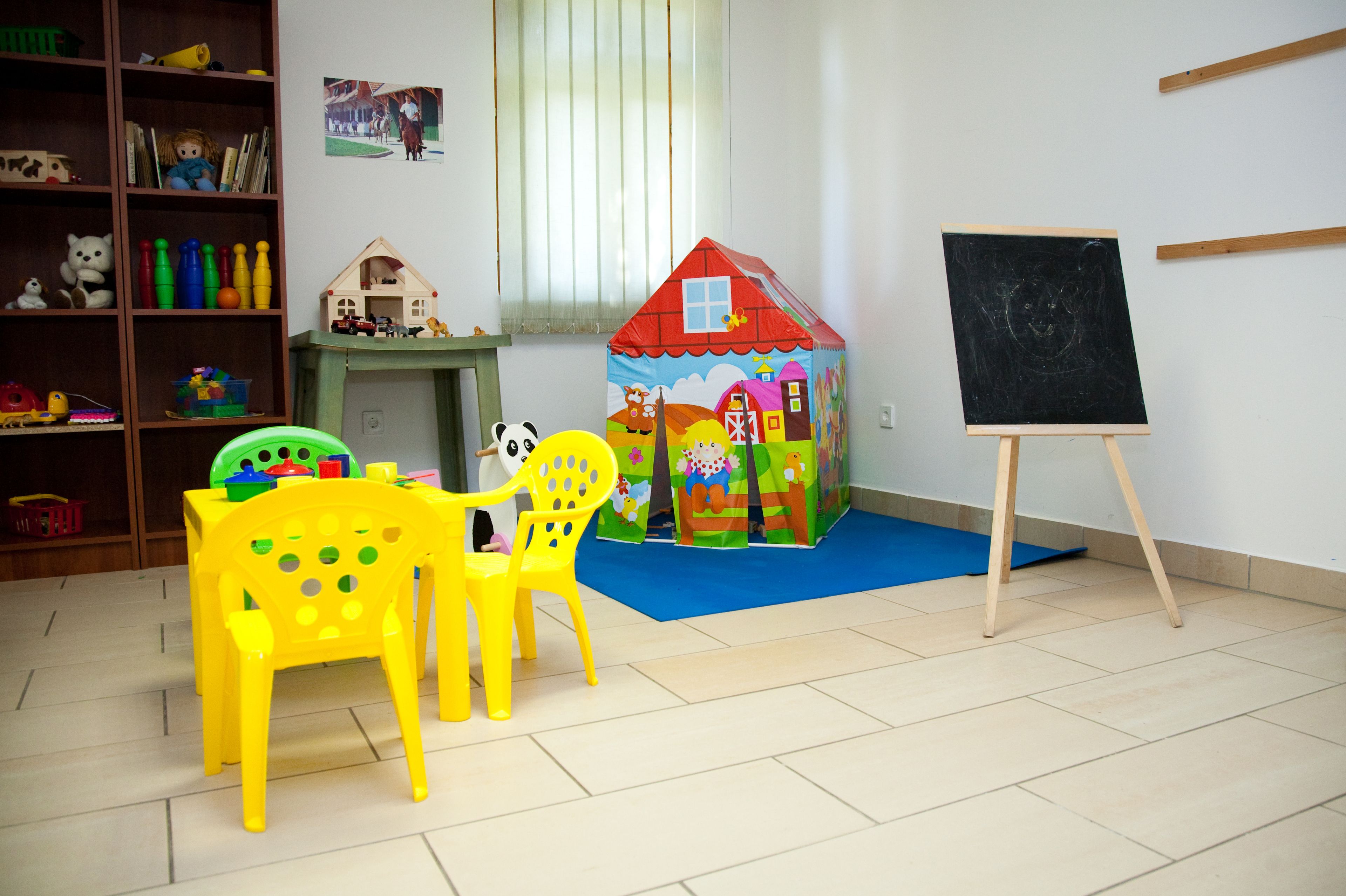 Una habitación con una casita de juegos, una pizarra y un estante lleno de juguetes.