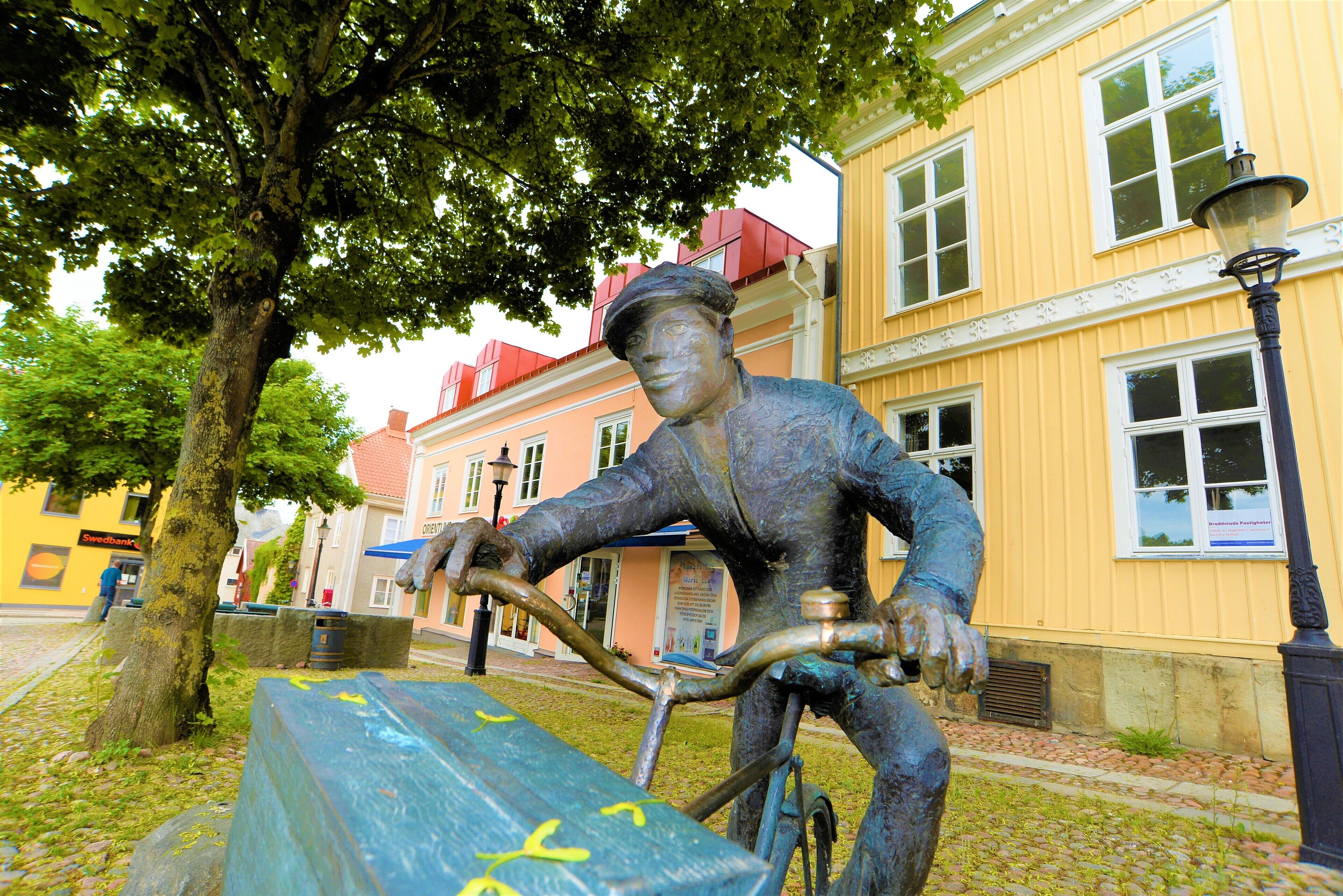 A statue of a man on a bicycle in front of a building with a yellow facade and red roof.