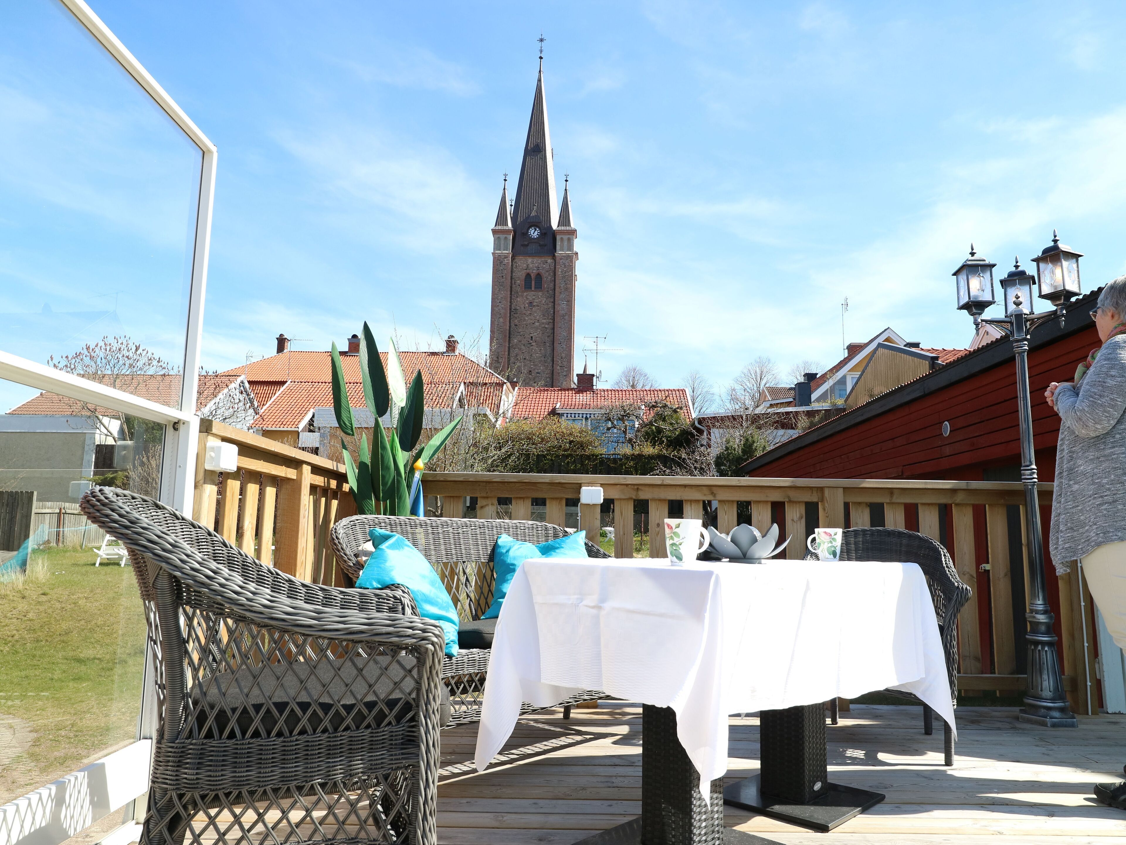 An outdoor patio with wicker furniture and a table, a church spire in the background, and a red-roofed building.