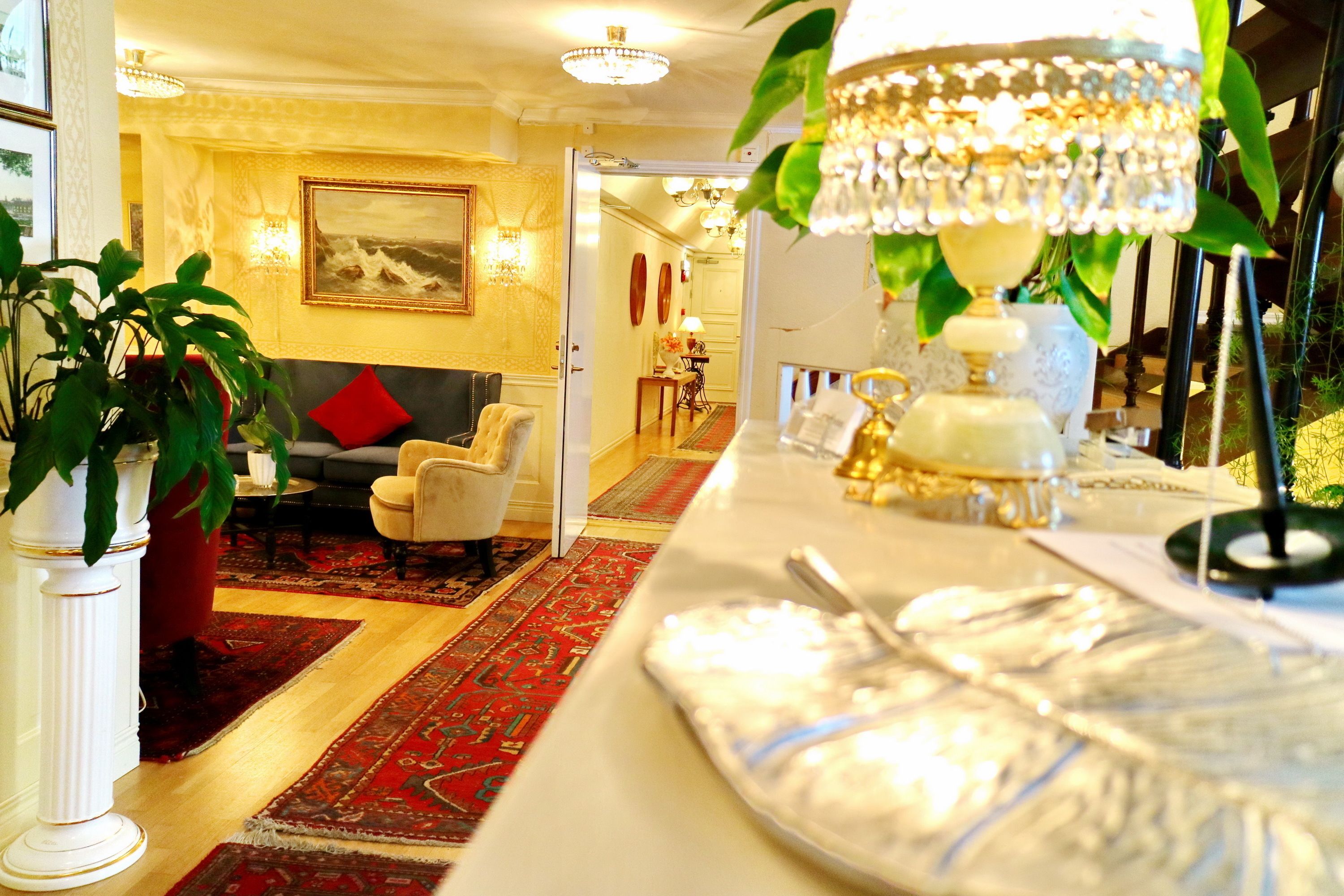 A well-lit hotel lobby with a red carpet, a sofa, a dining table with a chandelier, and a potted plant.