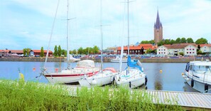 A marina with several boats docked, a church tower in the background, and a wooden dock in the foreground. - Vänerport Lakefront (Mariestad)