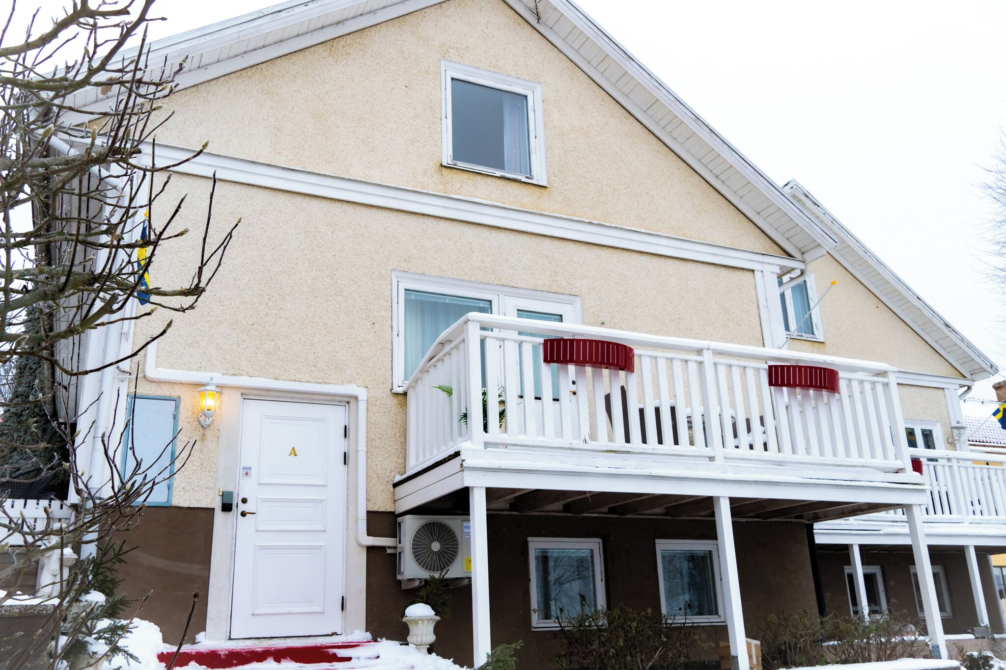 A two-story house with a white front door, a balcony with a red railing, and a small window above the door.