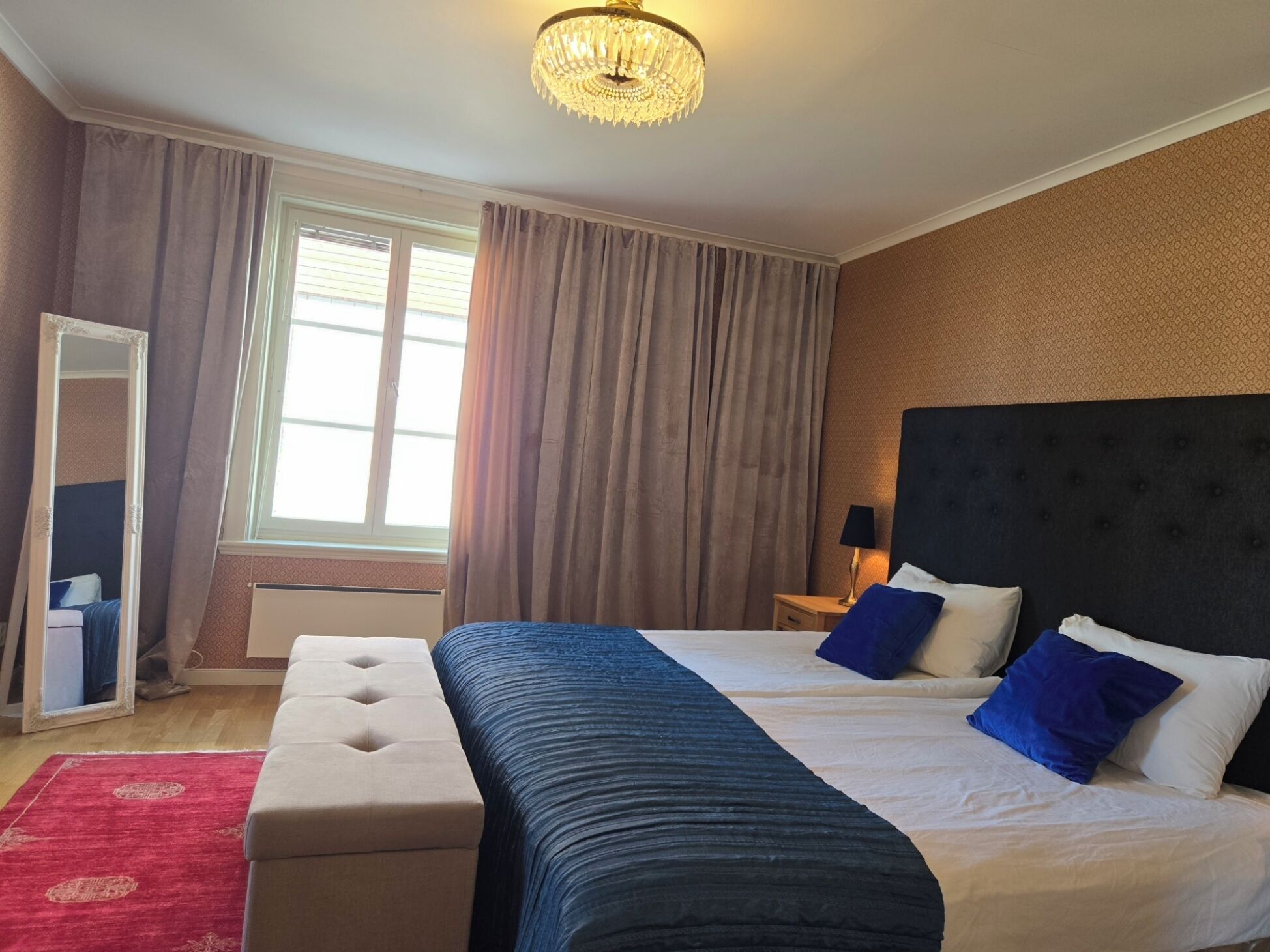 Habitación de hotel con una cama grande, una mesita de noche, un espejo y una alfombra roja.