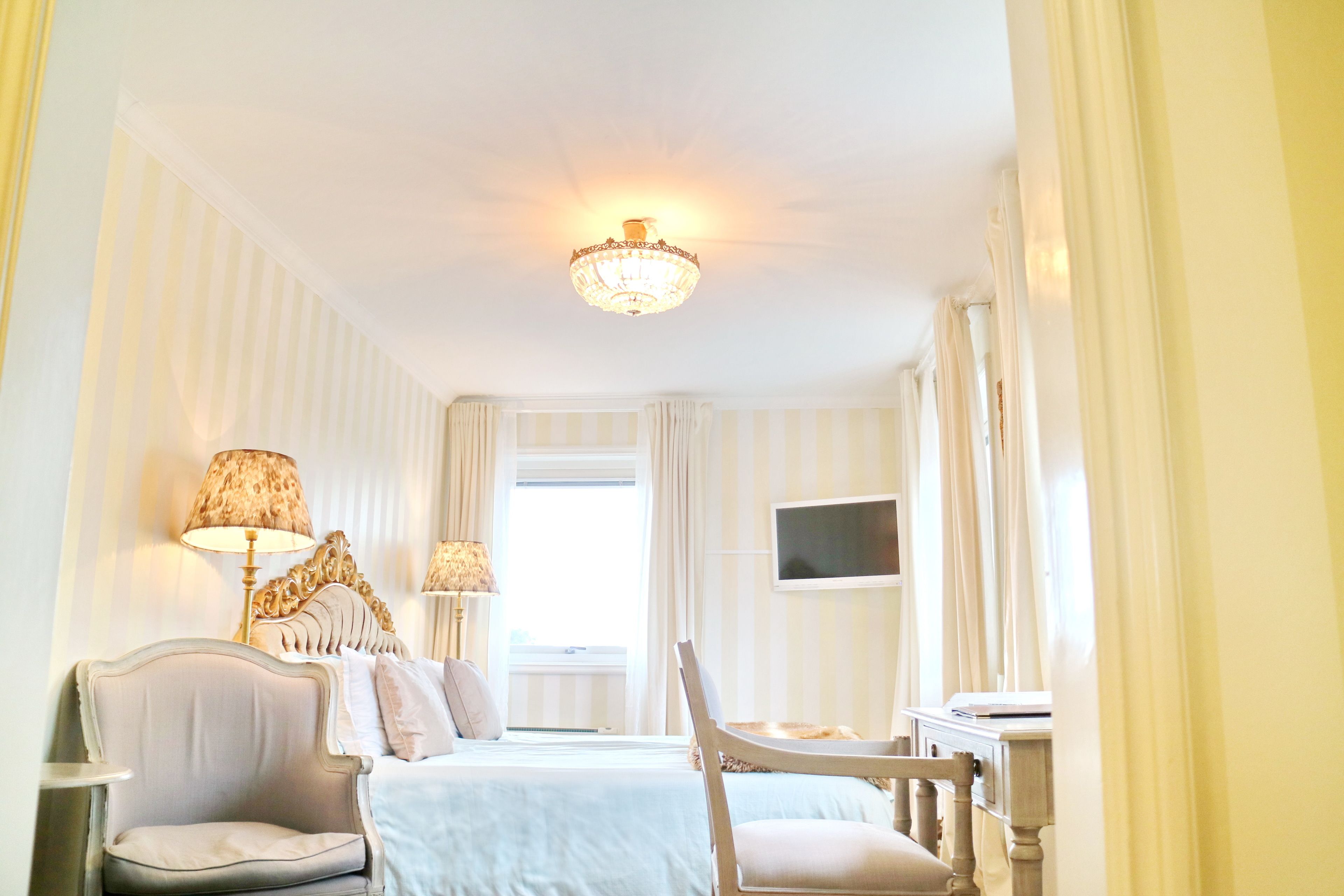 Una habitación de hotel con cama, dos sillas, escritorio, televisor y candelabro.
