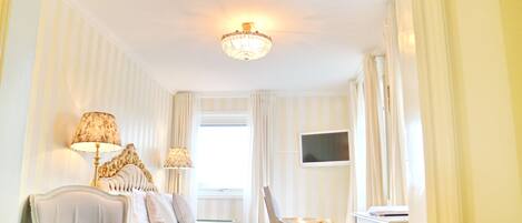 Una habitación de hotel con cama, dos sillas, escritorio, televisor y candelabro.