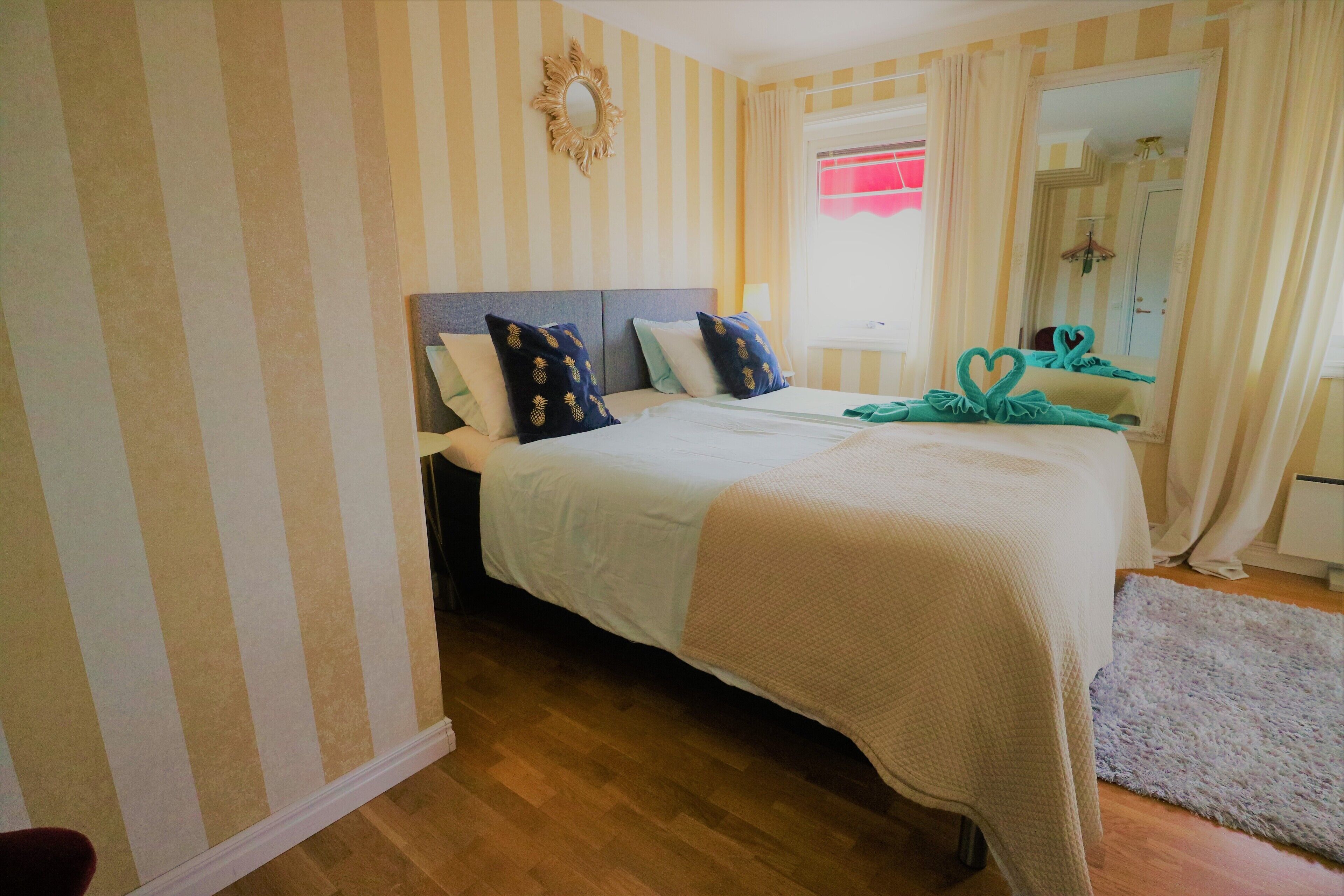 Habitación de hotel con cama, papel tapiz a rayas, espejo y ventana con cortinas.