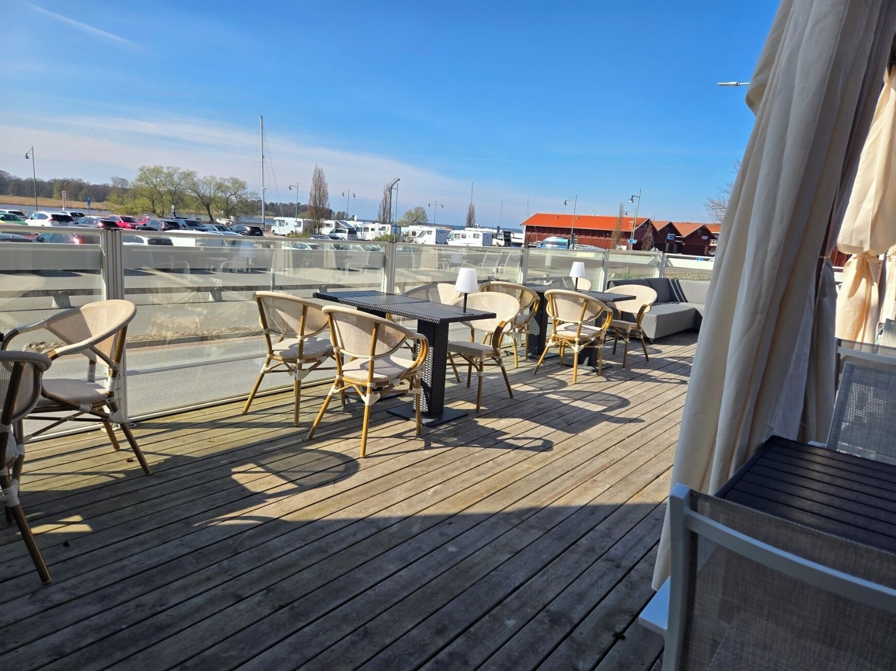 Une terrasse en bois avec des sièges extérieurs, une vue sur les voitures garées et, au fond, un bâtiment avec un toit orange.