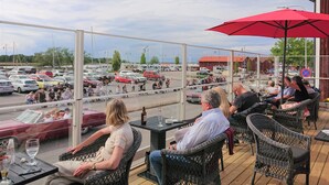 An outdoor seating area with wicker chairs and tables, overlooking a parking lot with various vehicles. - Vänerport Lakefront (Mariestad)